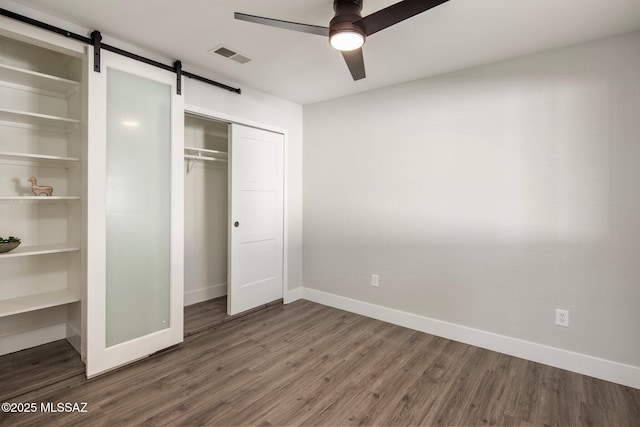 unfurnished bedroom featuring a barn door, dark hardwood / wood-style floors, ceiling fan, and a closet