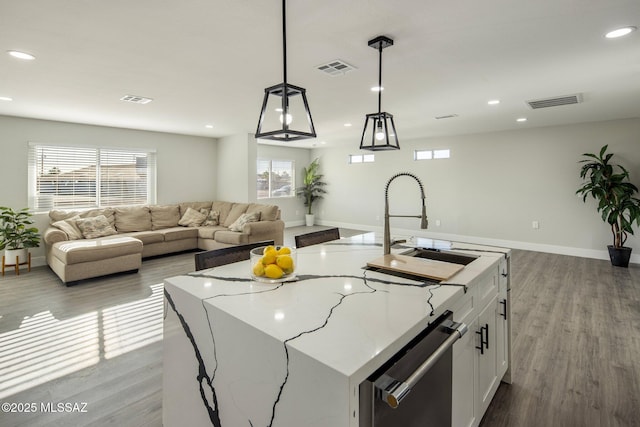 kitchen featuring white cabinetry, light stone counters, an island with sink, and hanging light fixtures