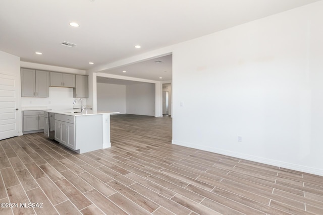 kitchen with gray cabinets, an island with sink, sink, and light hardwood / wood-style floors