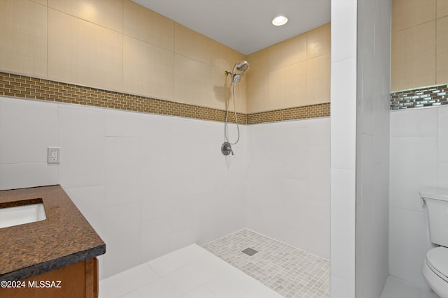 full bath with tile walls, tiled shower, vanity, and toilet