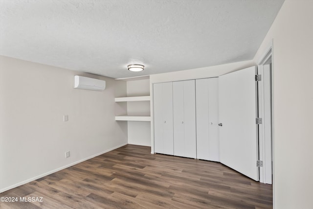 unfurnished bedroom with a wall mounted air conditioner, dark wood finished floors, a textured ceiling, and baseboards