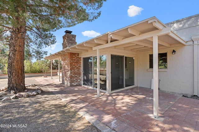 back of house featuring a patio area, a chimney, stucco siding, and brick siding