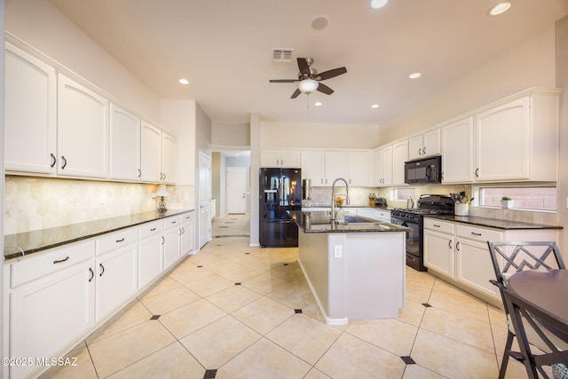 kitchen featuring black appliances, dark stone countertops, light tile patterned floors, a kitchen island with sink, and white cabinets