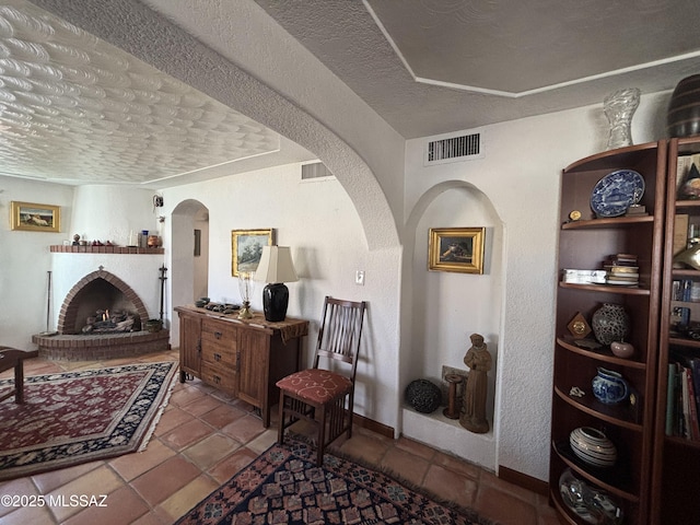 living area with a brick fireplace, a textured ceiling, and light tile patterned floors