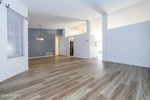 unfurnished living room with hardwood / wood-style floors, ceiling fan with notable chandelier, and vaulted ceiling