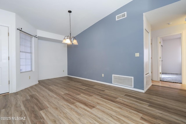 spare room featuring lofted ceiling, hardwood / wood-style floors, and an inviting chandelier