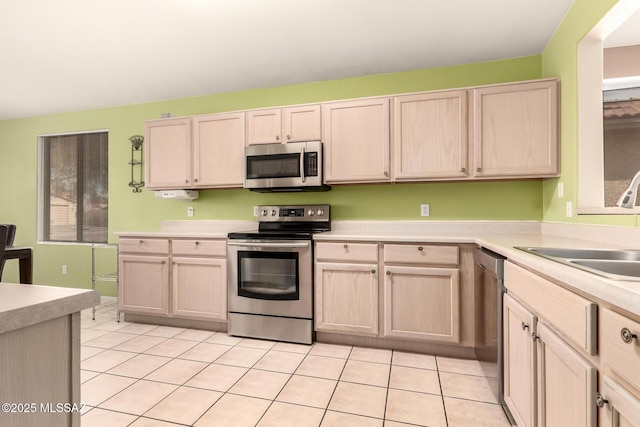 kitchen with stainless steel appliances, light brown cabinetry, sink, and light tile patterned floors