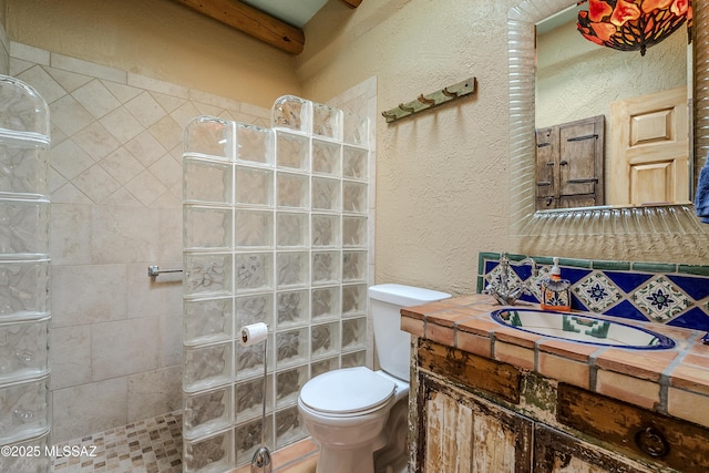 bathroom featuring vanity, a tile shower, and toilet