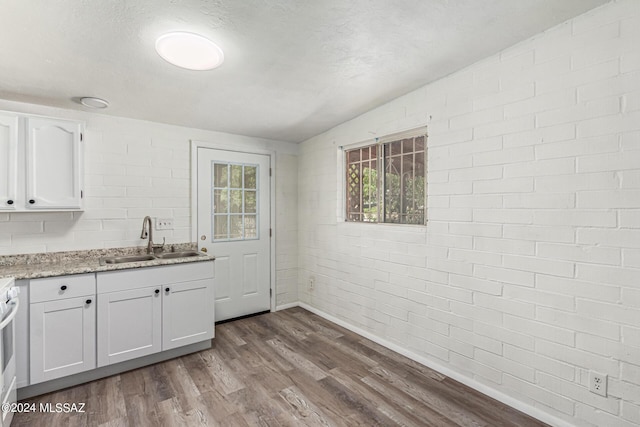 kitchen with sink, brick wall, white range, hardwood / wood-style floors, and white cabinets