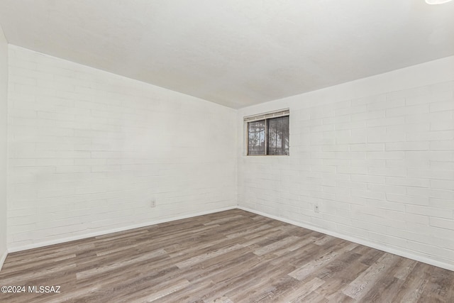 empty room featuring hardwood / wood-style flooring and brick wall