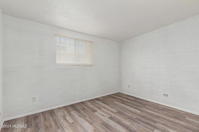 unfurnished room with hardwood / wood-style flooring and brick wall