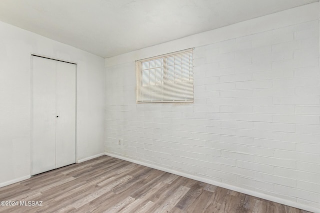 unfurnished bedroom featuring brick wall, a closet, and light wood-type flooring