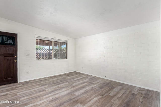 spare room with brick wall, light hardwood / wood-style floors, and vaulted ceiling