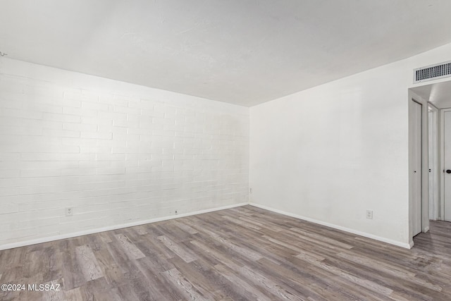 unfurnished room featuring brick wall and wood-type flooring