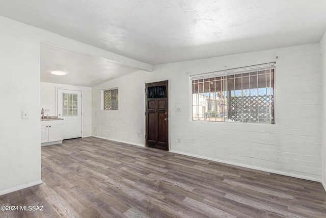 spare room with lofted ceiling with beams, wood-type flooring, brick wall, and sink