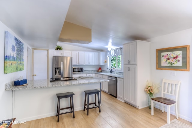 kitchen with sink, white cabinetry, light stone counters, appliances with stainless steel finishes, and a kitchen breakfast bar