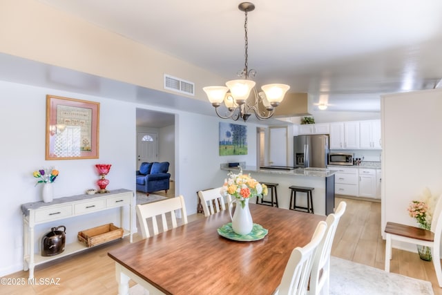 dining room featuring vaulted ceiling, an inviting chandelier, and light hardwood / wood-style floors