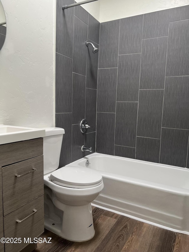 full bathroom featuring hardwood / wood-style flooring, vanity, tiled shower / bath combo, and toilet