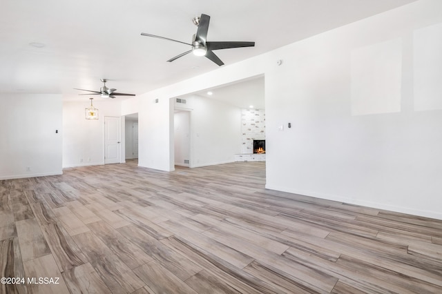 unfurnished living room featuring ceiling fan, a large fireplace, and light wood-type flooring