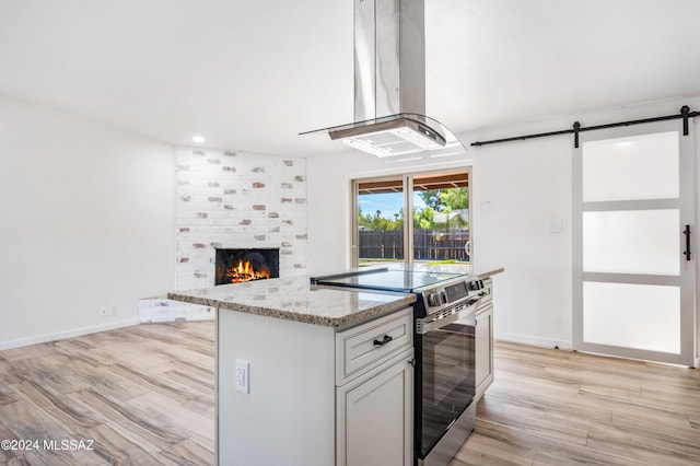 kitchen featuring light stone countertops, stainless steel range with electric cooktop, light hardwood / wood-style floors, and island exhaust hood