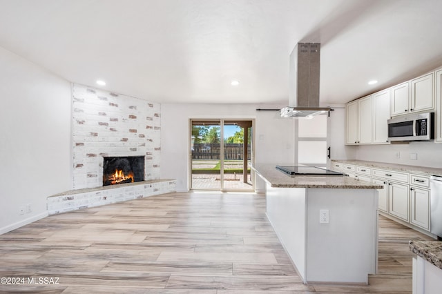 kitchen featuring a fireplace, white cabinets, island exhaust hood, black electric stovetop, and light stone countertops