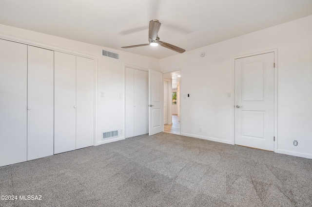 unfurnished bedroom with carpet floors, two closets, and ceiling fan