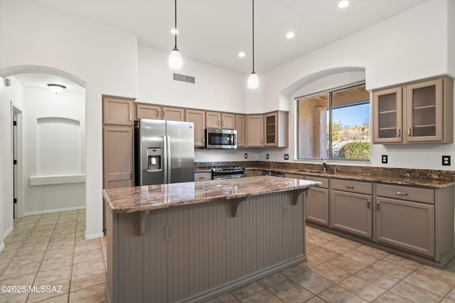 kitchen with sink, a center island, dark stone counters, pendant lighting, and stainless steel appliances