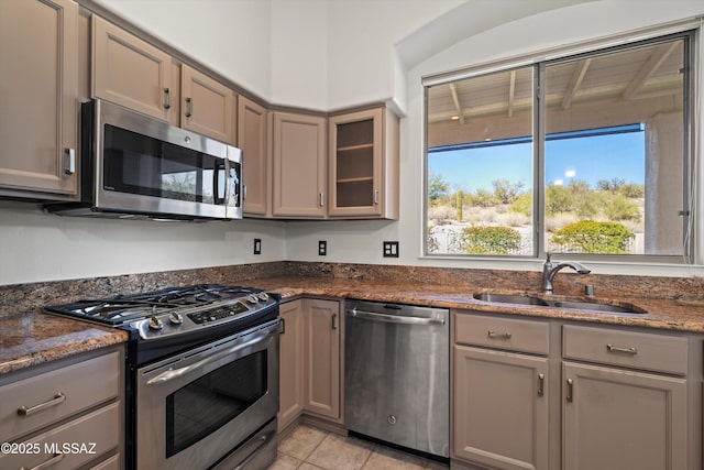 kitchen featuring stainless steel appliances, sink, dark stone countertops, and light tile patterned floors