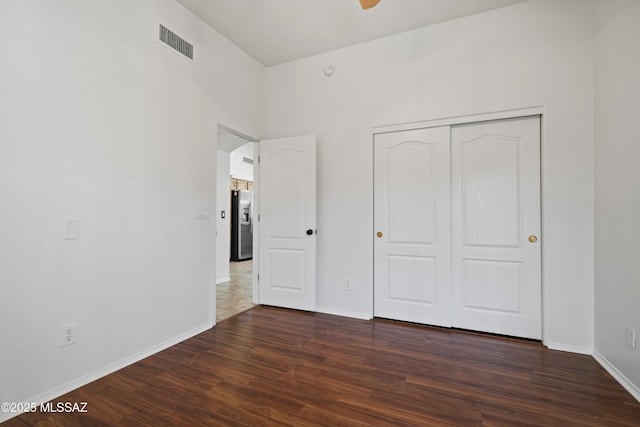 unfurnished bedroom featuring dark wood-type flooring, stainless steel fridge, and a closet