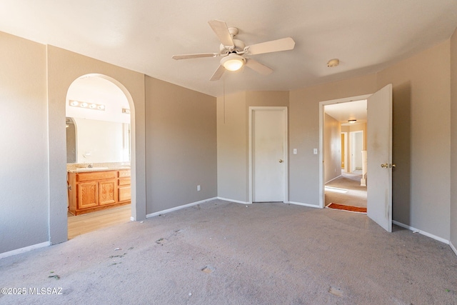 unfurnished bedroom featuring ceiling fan, sink, light carpet, and ensuite bath