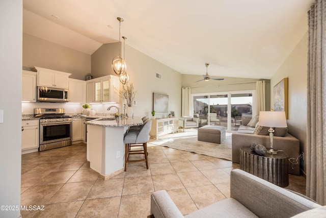 kitchen with light stone counters, white cabinetry, decorative light fixtures, appliances with stainless steel finishes, and a kitchen breakfast bar