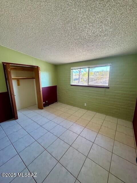 unfurnished bedroom featuring brick wall, a textured ceiling, and light tile patterned floors