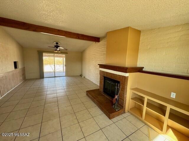 unfurnished living room featuring tile patterned flooring, ceiling fan, a brick fireplace, and a textured ceiling