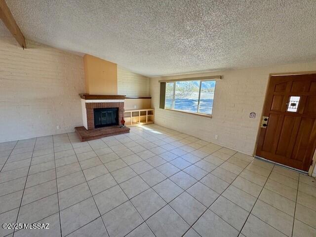 unfurnished living room with light tile patterned floors, a fireplace, a textured ceiling, and brick wall