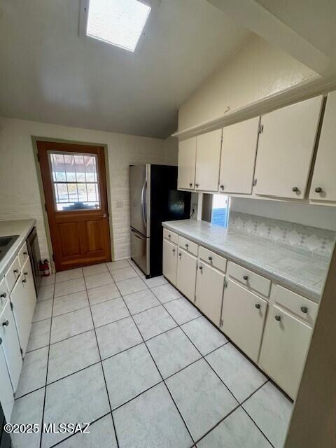 kitchen featuring white cabinetry, lofted ceiling, stainless steel fridge, and light tile patterned floors