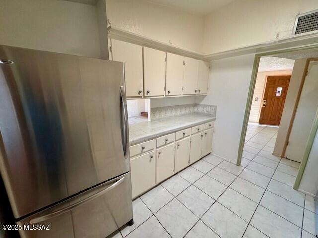 kitchen with stainless steel refrigerator, light tile patterned flooring, and white cabinets