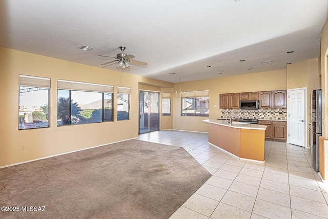 kitchen featuring light tile patterned flooring, tasteful backsplash, a kitchen island with sink, ceiling fan, and stainless steel appliances