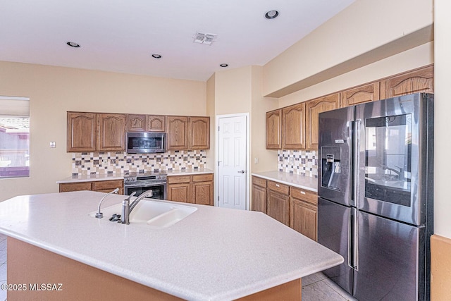 kitchen with appliances with stainless steel finishes, sink, a center island with sink, and backsplash