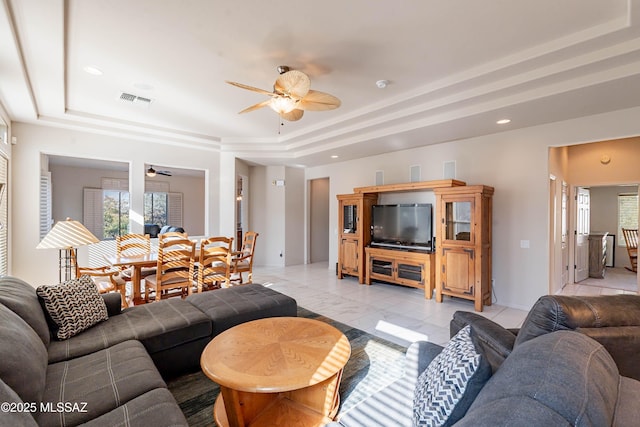 tiled living room featuring ceiling fan and a tray ceiling