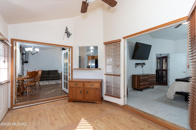 interior space featuring high vaulted ceiling, ceiling fan with notable chandelier, and light hardwood / wood-style floors