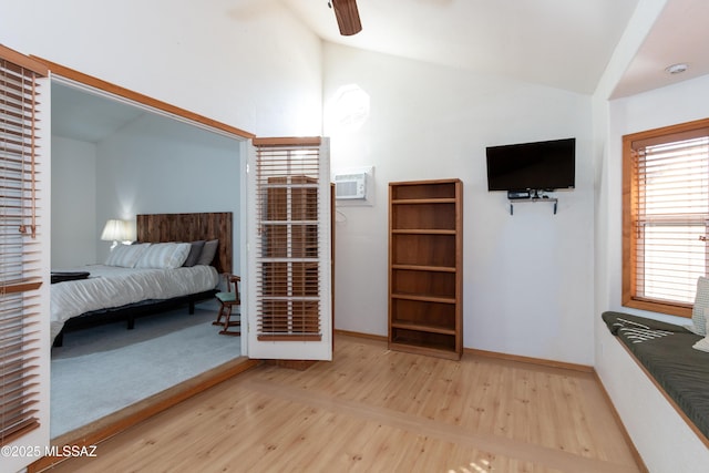 bedroom with ceiling fan, a wall mounted air conditioner, light hardwood / wood-style floors, and vaulted ceiling