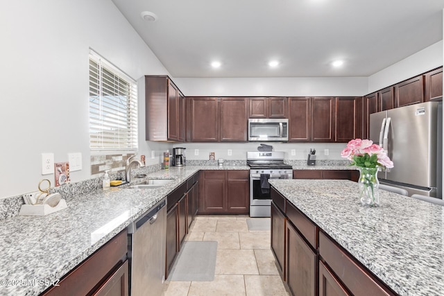 kitchen with stainless steel appliances, light stone countertops, sink, and light tile patterned floors