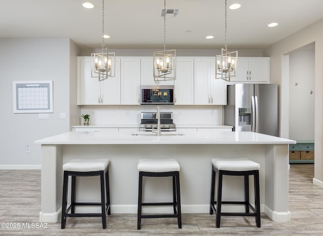 kitchen with appliances with stainless steel finishes, a center island with sink, and white cabinets