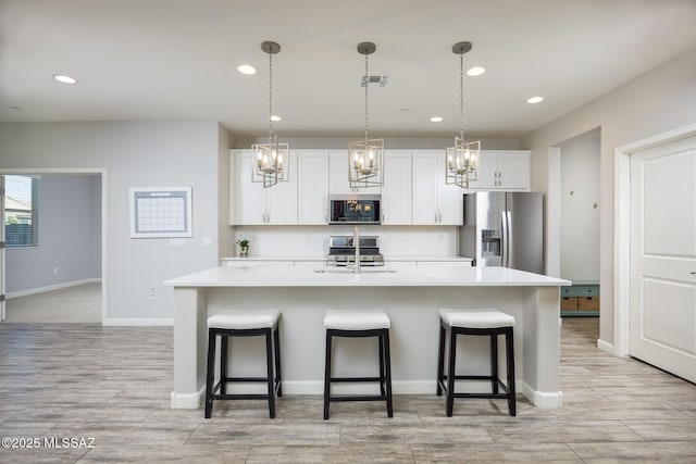 kitchen featuring white cabinetry, appliances with stainless steel finishes, a breakfast bar area, and a center island with sink