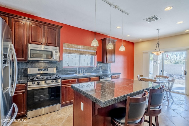 kitchen featuring sink, a breakfast bar area, stainless steel appliances, a kitchen island, and decorative light fixtures