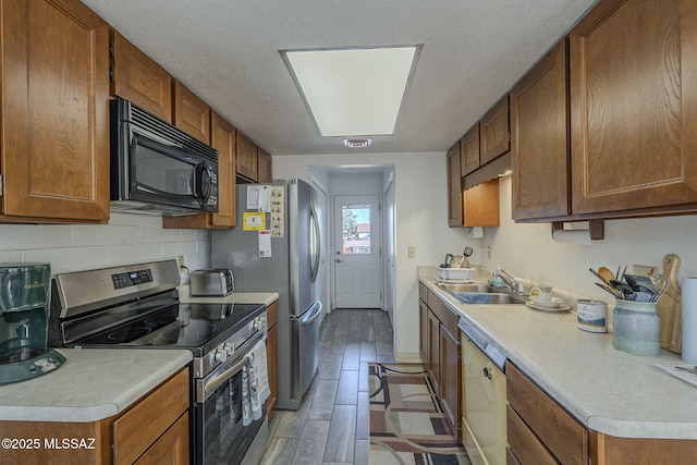 kitchen with sink, dishwashing machine, stainless steel range with electric cooktop, decorative backsplash, and light wood-type flooring