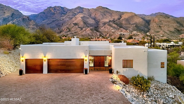 pueblo-style house with decorative driveway, a chimney, stucco siding, an attached garage, and a mountain view