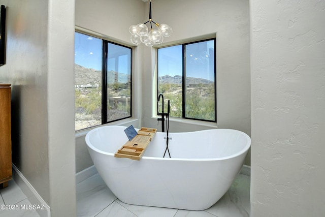 full bath with marble finish floor, a textured wall, a freestanding bath, and an inviting chandelier