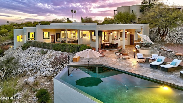 back of property at dusk featuring stucco siding, an outdoor pool, and a patio