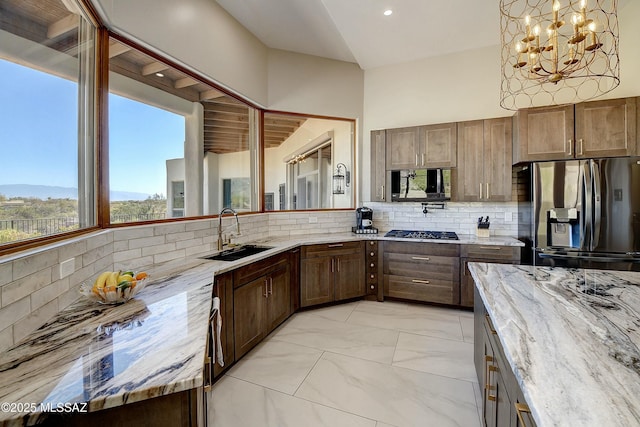 kitchen with stainless steel appliances, a sink, backsplash, and light stone countertops